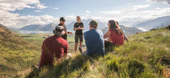 Six people chat on a hillside above a lake